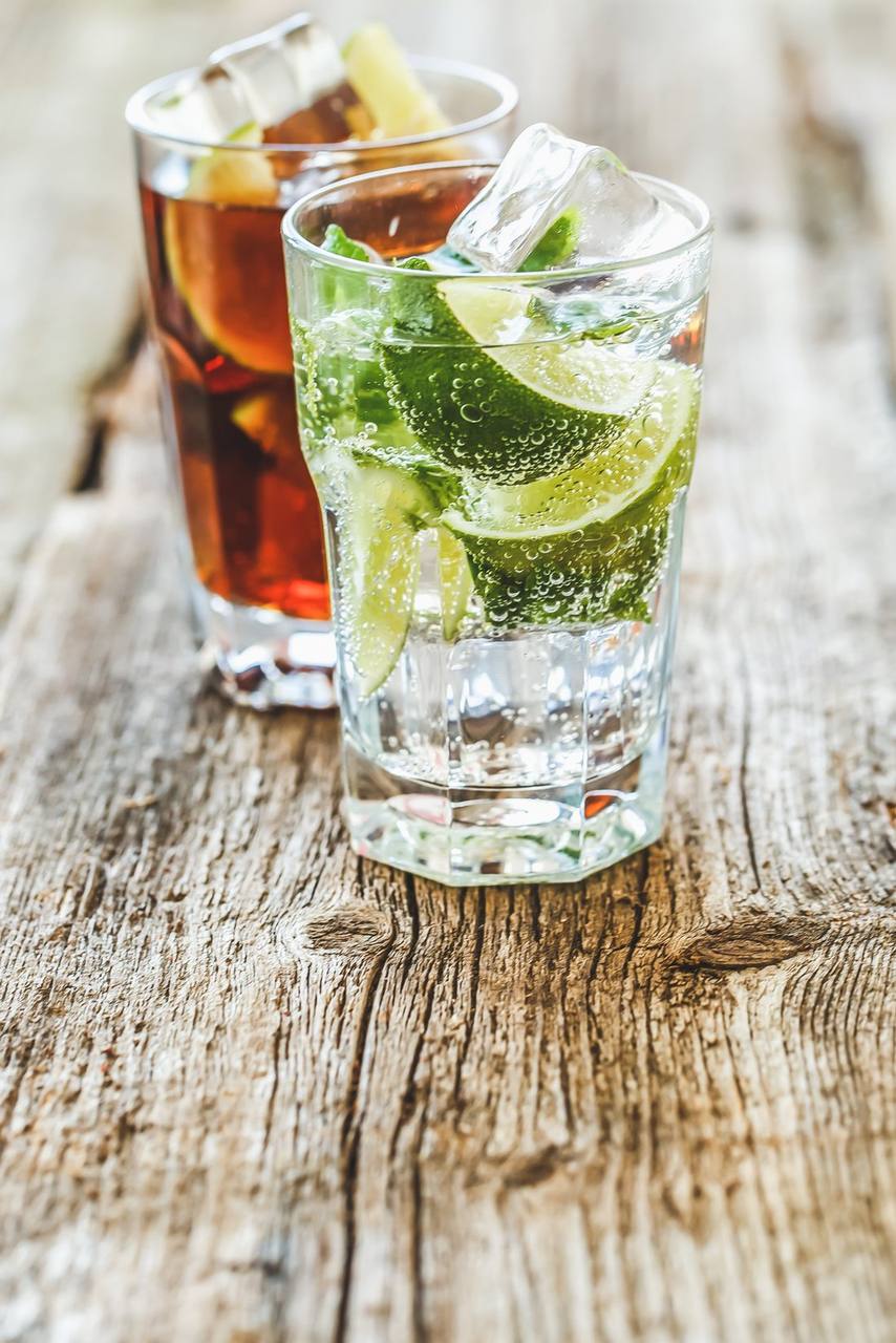 Zwei Longdrinks mit Eis, Limette und Minze auf einem Holztisch