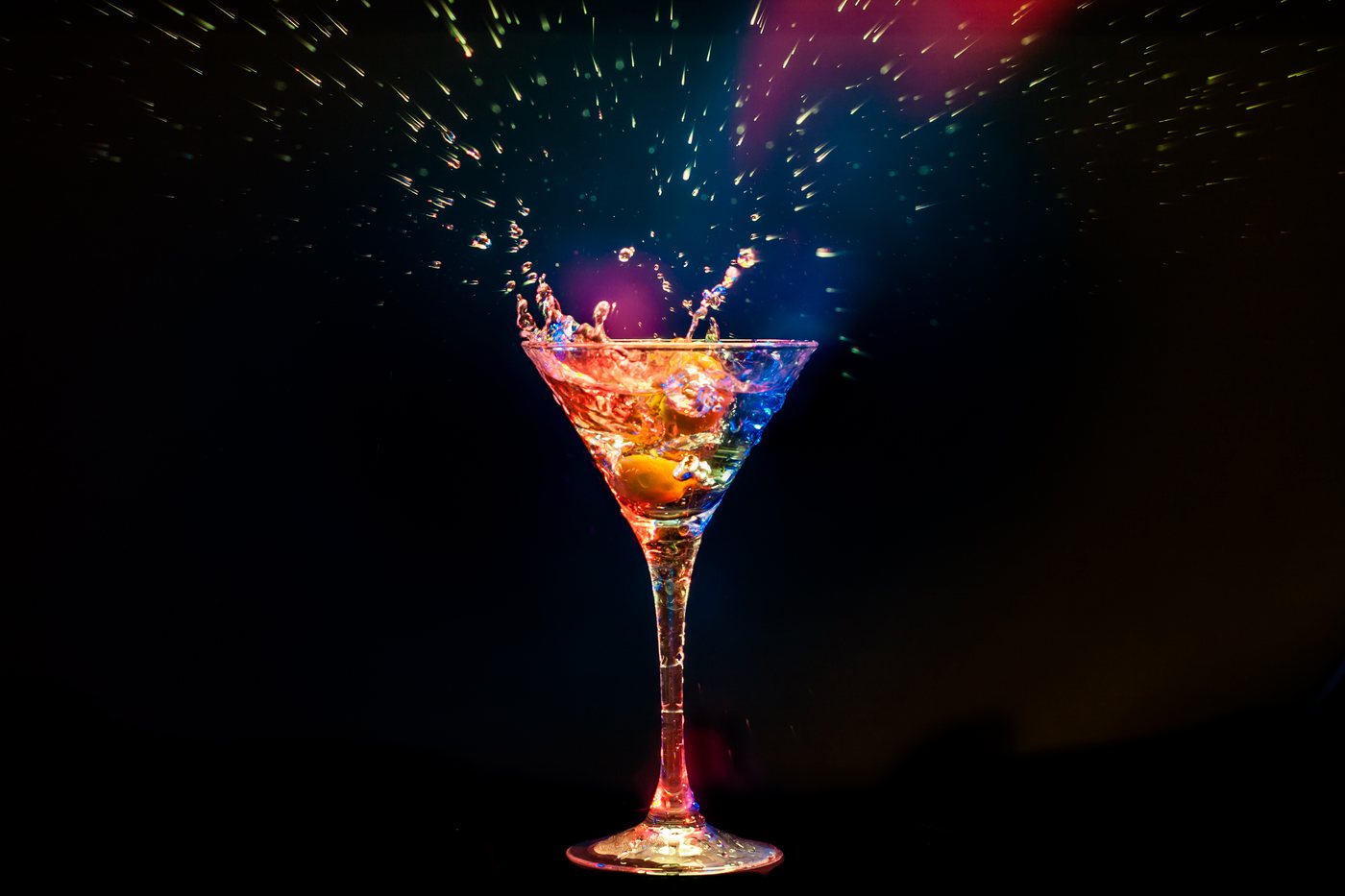 Cocktailglas mit farbigem Drink und spritzender Flüssigkeit vor dunklem Hintergrund